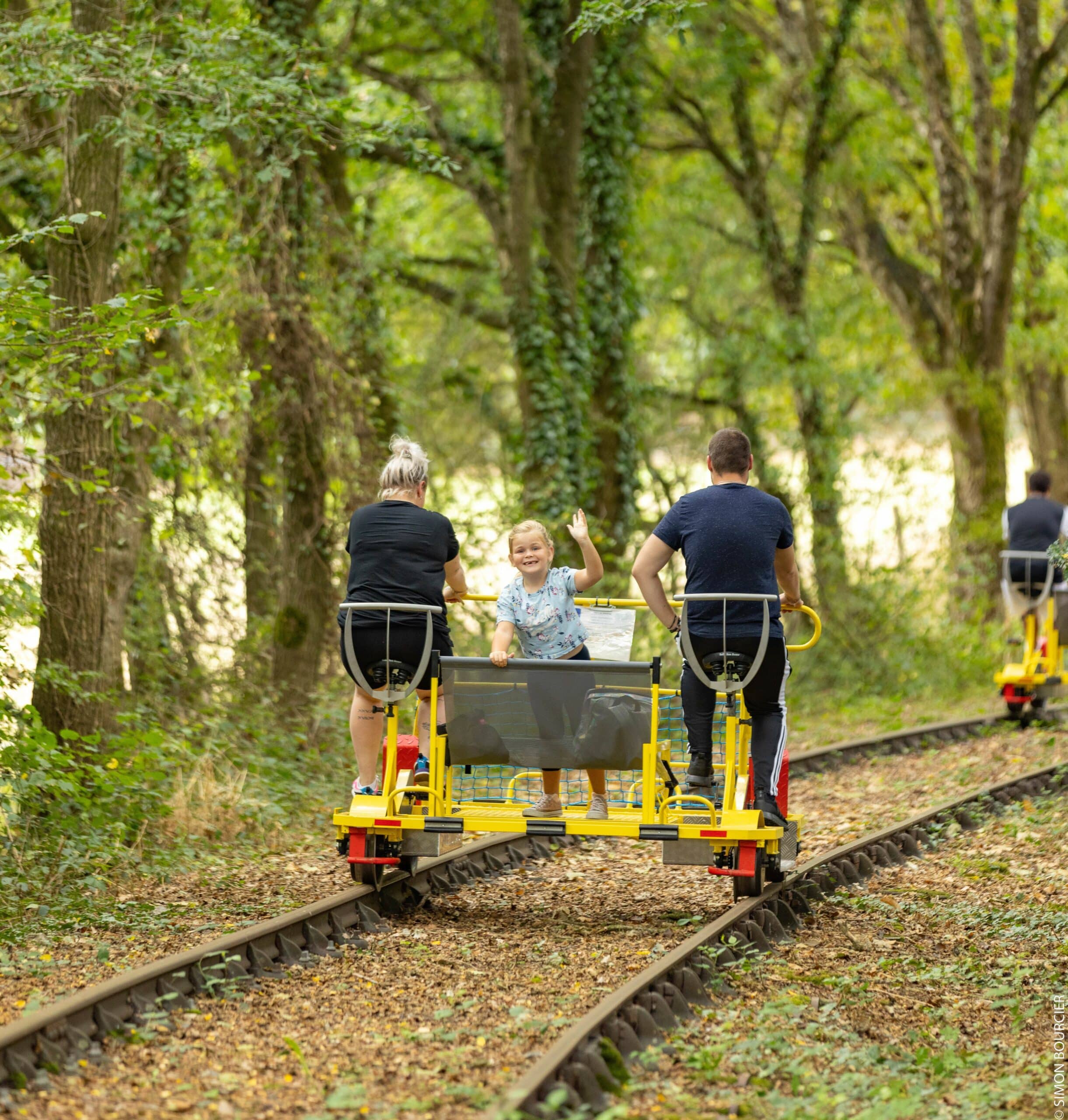 famille sur un vélorail avec petite fille qui fait coucou